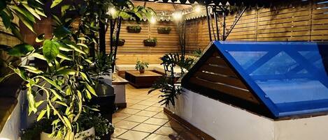 A rooftop patio with a wooden deck, potted plants, a seating area, and a glass enclosure.