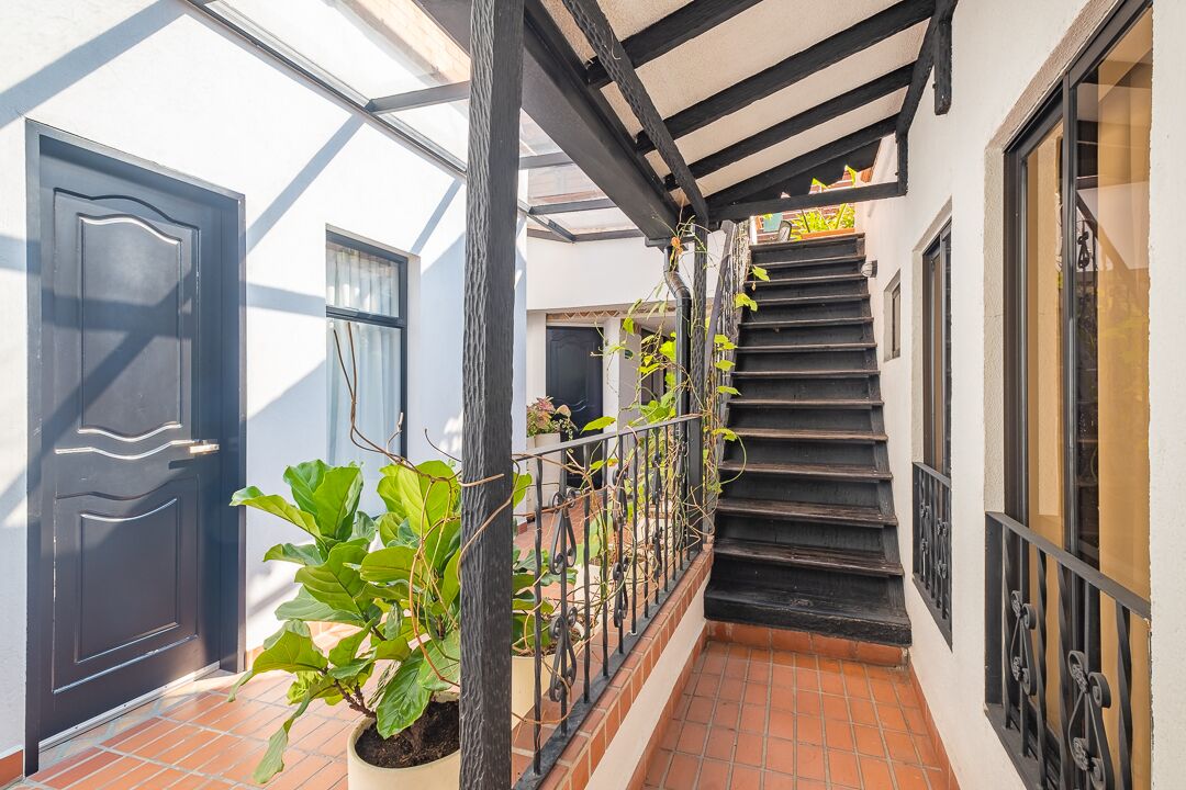 A covered outdoor staircase with a metal railing, leading to a door with a sign above it.
