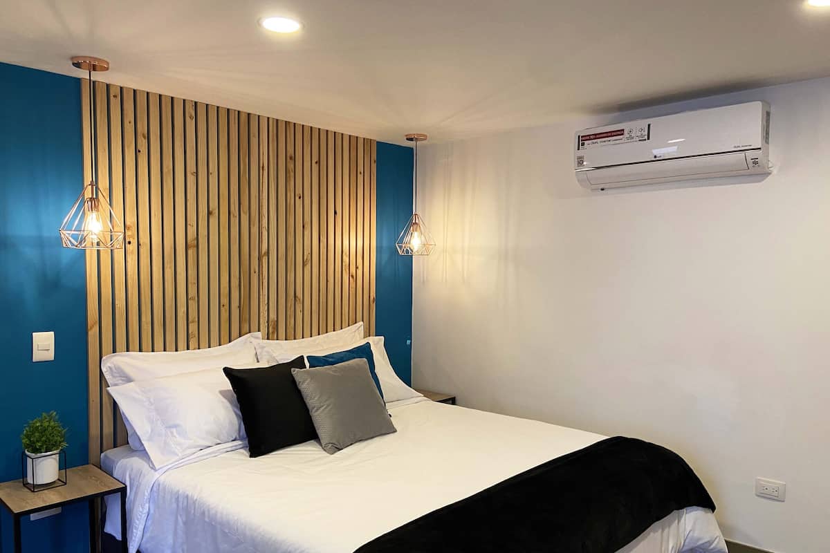 A bedroom with a bed, bedside tables, a wall-mounted air conditioner, and a wooden slat wall design.
