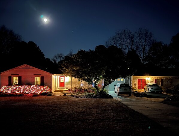 Une maison avec une porte rouge et un garage, entourée d’une pelouse et d’arbres.