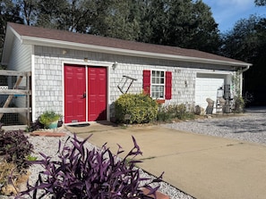 A single-story building with a red door and white garage door, surrounded by gravel and plants.