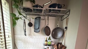 A compact kitchen with a gas stove, hanging pots, a spice rack, and a potted plant.