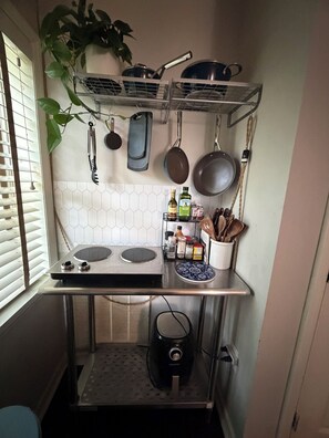 Une cuisine compacte équipée d’une cuisinière à gaz, de casseroles suspendues, d’un porte-épices et d’une plante en pot.