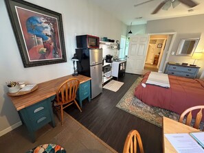Una habitación pequeña con kitchenette, una cama, un escritorio y una silla.