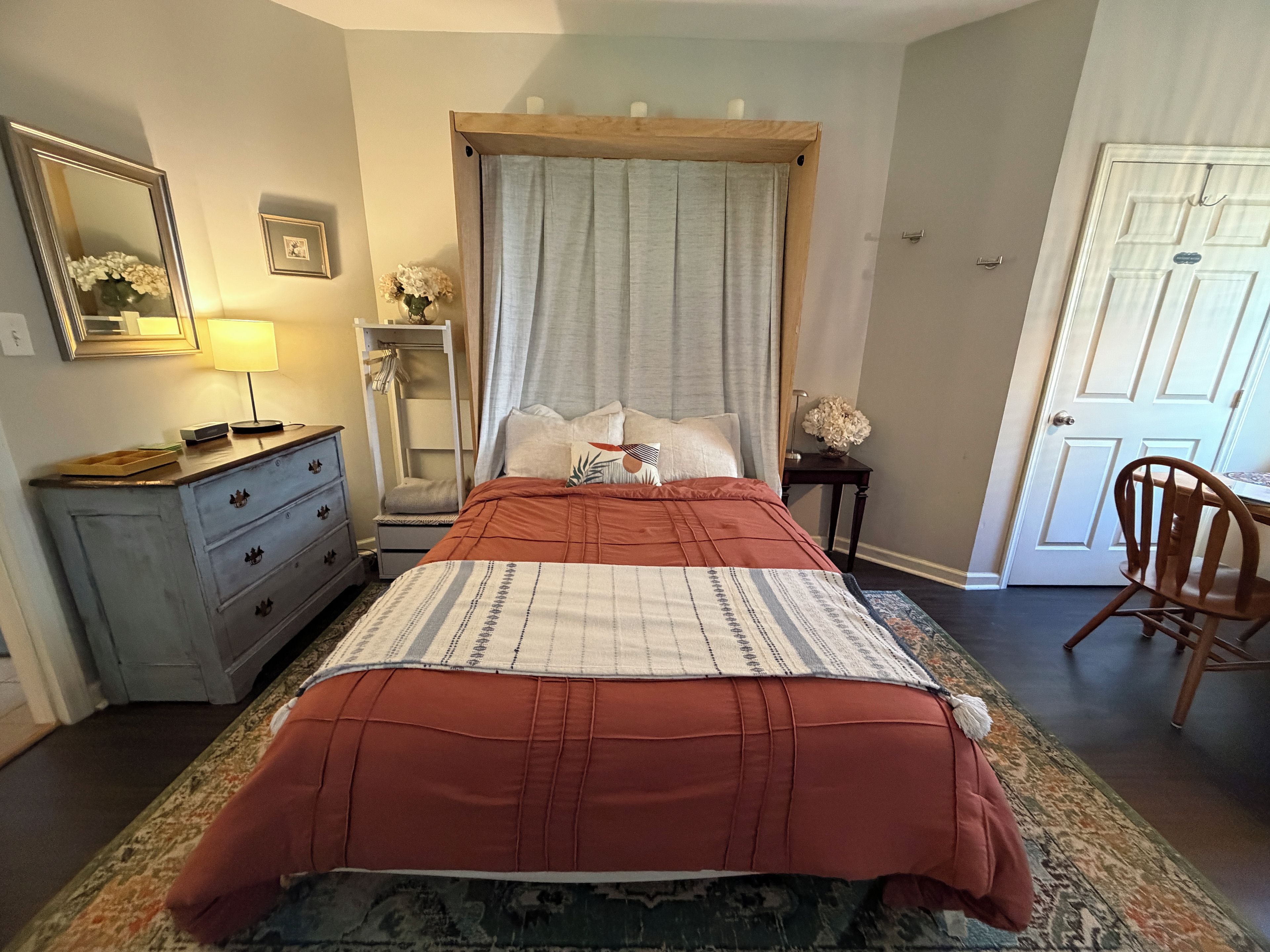 Une chambre à coucher avec un lit, une commode, un miroir, une porte et une chaise.