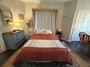 Un dormitorio con una cama, un tocador, un espejo, una puerta y una silla.