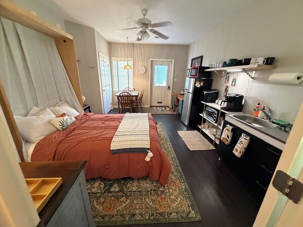 Una habitación de hotel compacta con cama, kitchenette, comedor y baño.