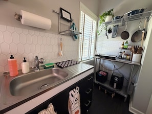 A kitchen with a double sink, a hanging rack with pots and pans, and a window with blinds.