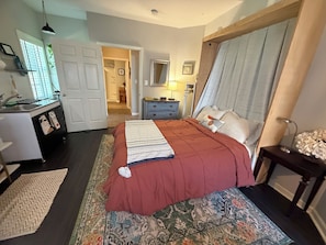 A bedroom with a bed, bedside table, lamp, and a view into the bathroom.