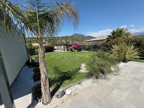 A well-maintained garden with a lawn, palm trees, and a patio area. - 3-Bedroom Villa with Private Pool in a Quiet Location with Mountain Views; Air-Conditioned / Fiber Optic Internet (Bastelicaccia)