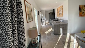 A modern kitchen with a central island, a dining area with a table, and a hallway with patterned curtains and artwork.