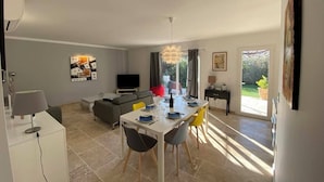 A modern living room with a dining area, a sofa, a TV, and a large window.
