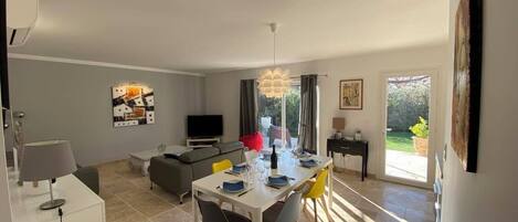En moderne stue med spiseplads, sofa, fjernsyn og et stort vindue.
