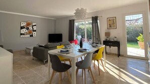 A dining area with a table set for four, a sofa, a TV, and a window with curtains.