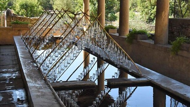 A wooden bridge with glass bottles suspended above a body of water.