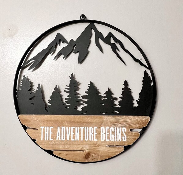 A circular wall decoration with a mountain silhouette and the text "THE ADVENTURE BEGINS" at the bottom.