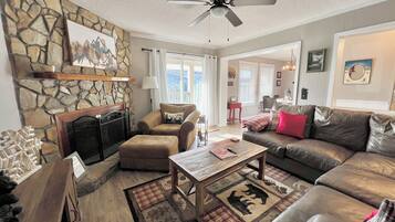 A cozy living room with a fireplace, stone wall, leather sofas, and a ceiling fan.