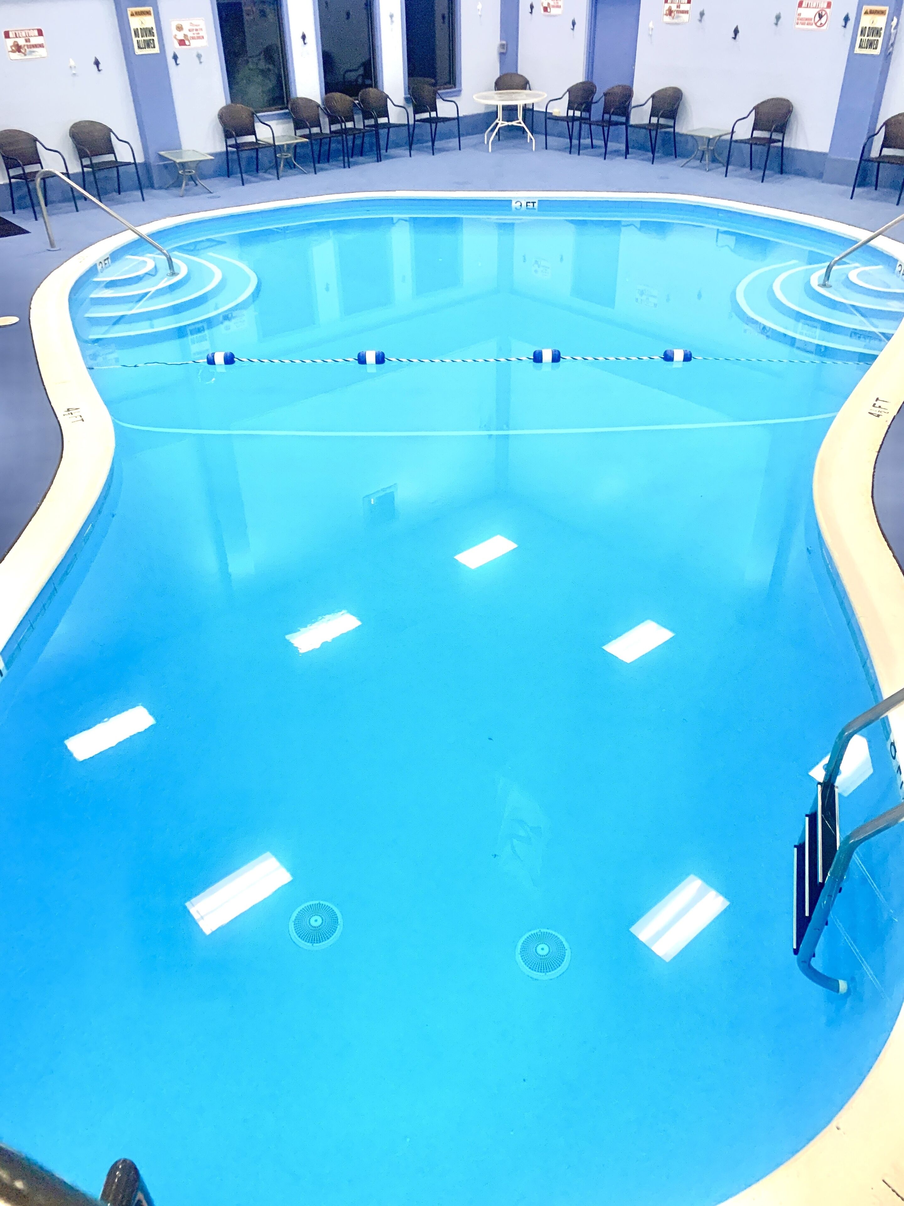 Une grande piscine intérieure dotée de plusieurs couloirs, entourée de chaises longues et de tables.
