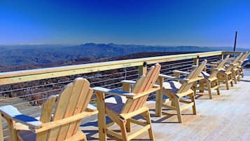 A wooden deck with Adirondack chairs overlooking a mountainous landscape.