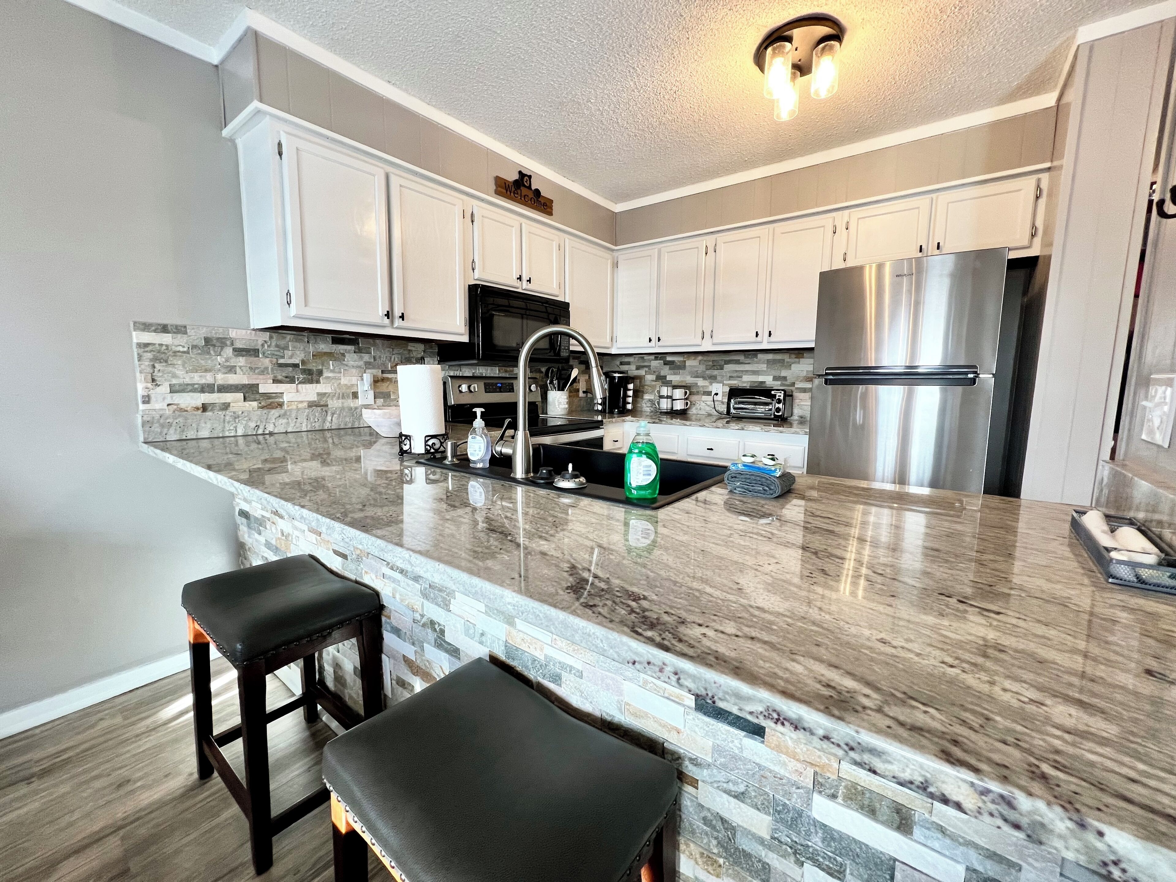 A modern kitchen with white cabinets, a granite countertop, a stainless steel refrigerator, and a built-in oven.
