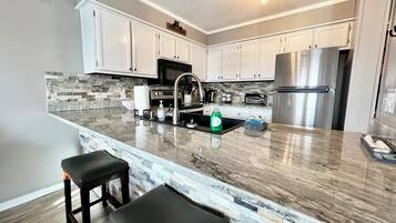 A modern kitchen with white cabinets, a granite countertop, a stainless steel refrigerator, and a built-in oven.