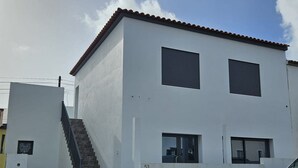 Un bâtiment moderne à deux étages, avec une façade blanche, un toit recouvert de tuiles et un escalier apparent menant à l’entrée.