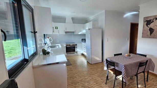 Une cuisine moderne avec des meubles blancs, une table à manger recouverte d’une nappe à carreaux et une carte du monde accrochée au mur.