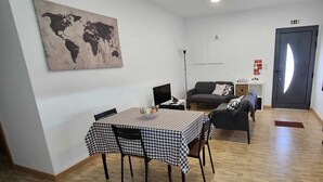 Une pièce comprenant une table à manger recouverte d’une nappe à carreaux, un canapé, une carte du monde accrochée au mur et une porte avec un panneau indiquant la sortie.