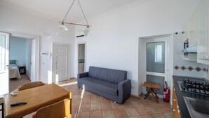 Ett kompakt bostadsutrymme med en matplats, en soffa, ett kök med en gasspis och en dörr som leder till ett annat rum.