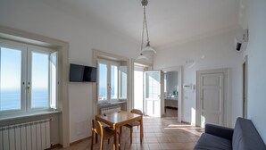 Ett rymligt vardagsrum med en soffa, ett matbord med stolar, en tv som är monterad på väggen och stora fönster med fin utsikt.