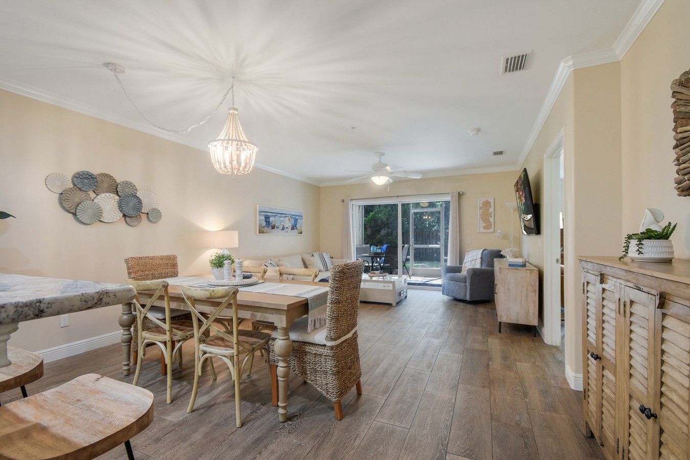 A dining area with a table and chairs, a chandelier, and a view through a glass door to an outdoor space.