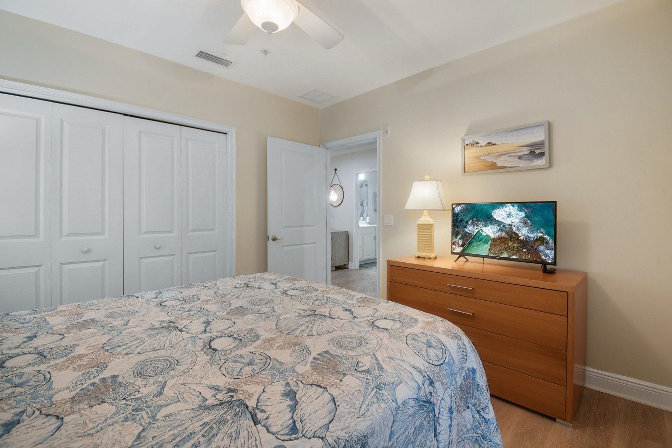 Une chambre à coucher avec un lit, une commode, un tableau et un ventilateur de plafond.