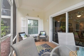 A covered patio area with wicker furniture, a glass table, and a view of the outdoors. - Ocean Reef 104 - intimate condo with pool (St Augustine Beach)