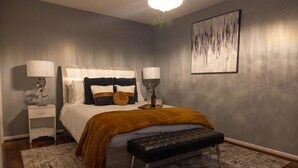 Une chambre à coucher avec un lit, des tables de chevet, un banc et un tableau accroché au mur.