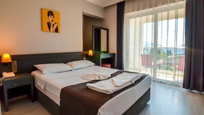Ein Hotelzimmer mit einem großen Bett, einem Schreibtisch, einem Stuhl, einer Lampe, einem Telefon, einem Spiegel und einem Fenster mit Vorhängen.