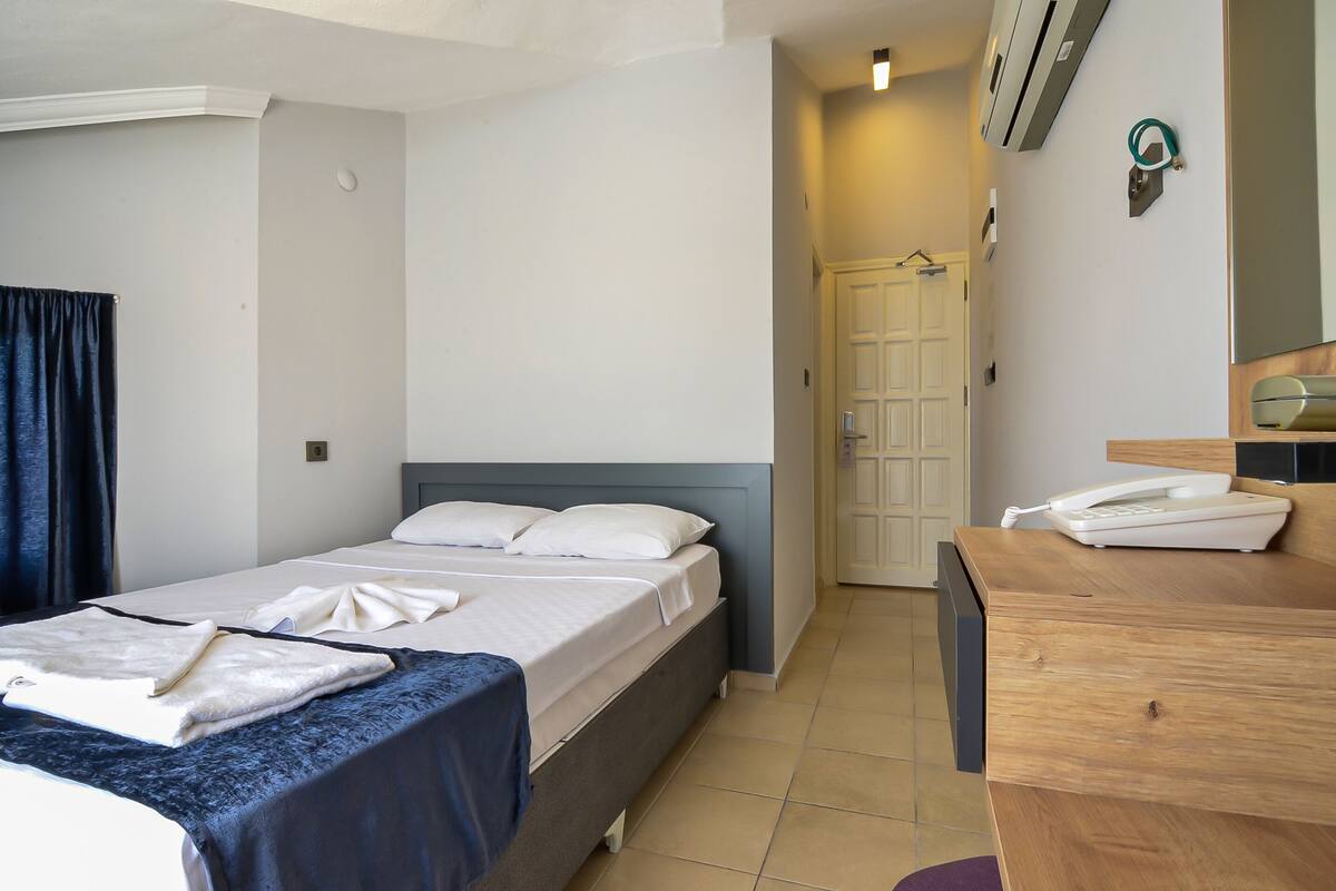 A hotel room with two beds, a wooden desk with a telephone, and a door leading to another room.