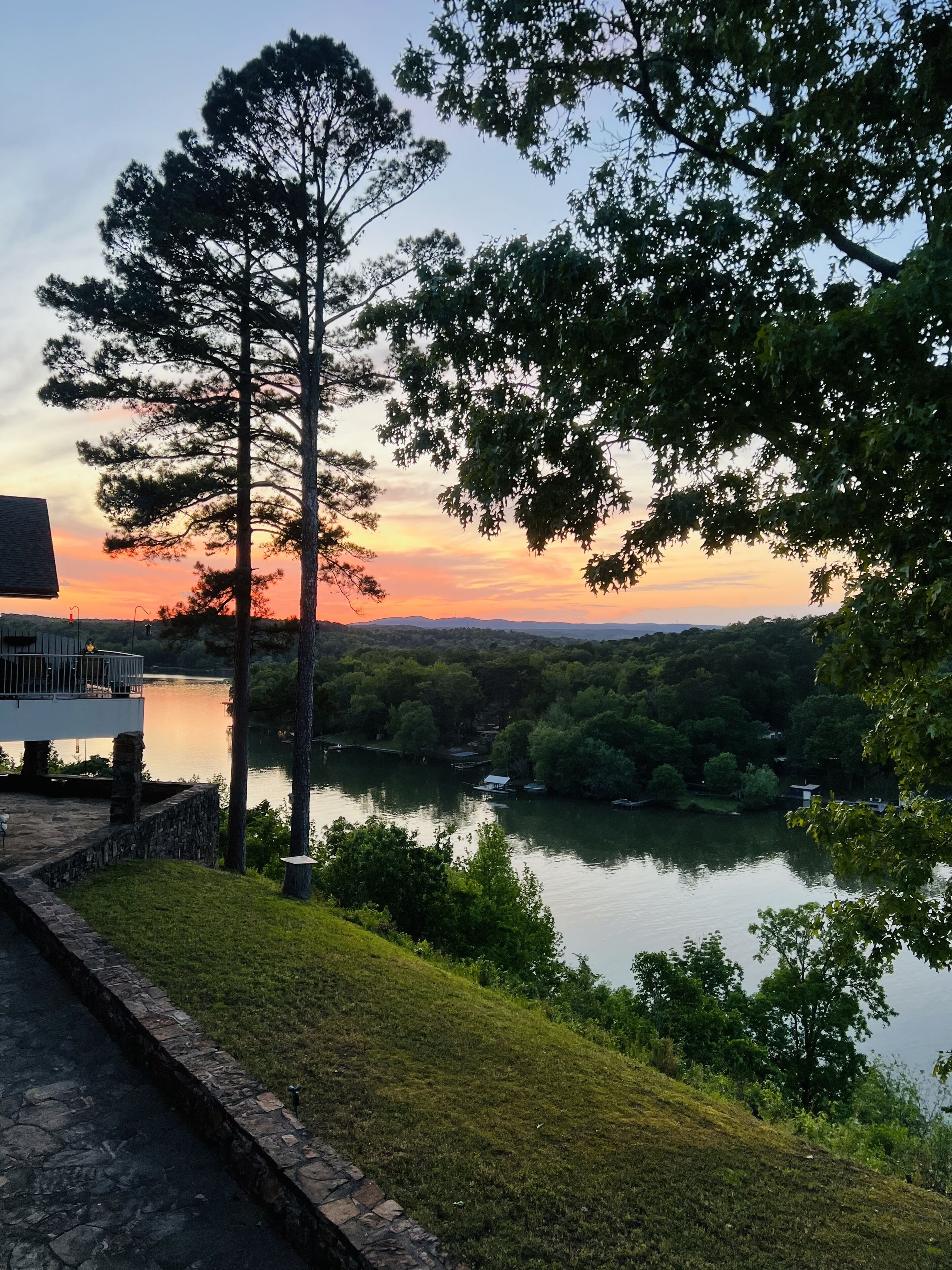 A lakeside view with a stone pathway leading to a building with a balcony overlooking the water.