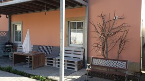 Ein Sitzbereich im Freien mit einer Holzbank, einem Tisch mit einer Schüssel und einem weißen Sonnenschirm.