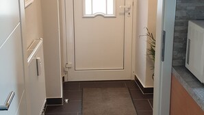 Ein Flur, der zu einer Tür mit Fenster, einem Heizkörper, einer kleinen Stufe und einer Pflanze führt.