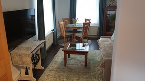 Ein Wohnzimmer mit Fernseher, Esstisch mit Stühlen, einer Couch und einem Schrank.
