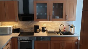 Eine kompakte Küche mit Holzausstattung, einer Mikrowelle, einem Toaster, einer Kaffeemaschine, einem Wasserkocher und einem Geschirrspüler.