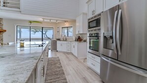 A modern kitchen with a large stainless steel refrigerator, white cabinetry, and a marble countertop. - Secluded Waterfront Bay Home! (Eastpoint)