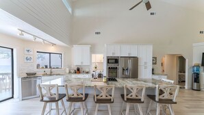 A spacious kitchen with a large island, white cabinetry, stainless steel appliances, and a bar area with wooden chairs. - Secluded Waterfront Bay Home! (Eastpoint)