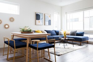 A modern living room with a blue sofa, wooden dining table, and matching chairs. - Walk to Restaurants from a Designer Cap Hill Home (Seattle)
