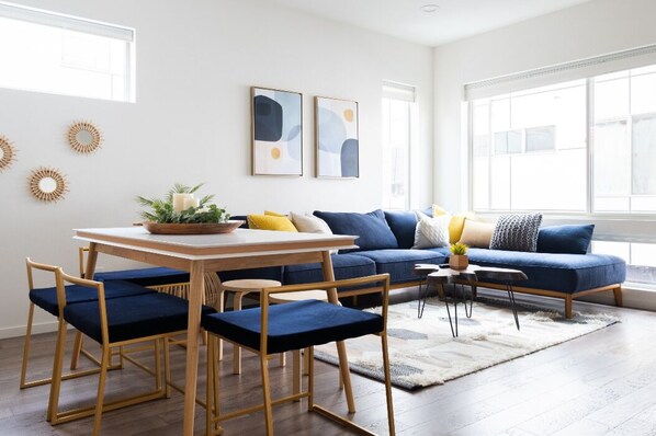 A modern living room with a blue sofa, wooden dining table, and matching chairs.