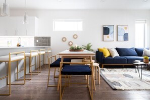 A modern kitchen with white cabinets, a dining table with chairs, and a blue sofa with cushions.