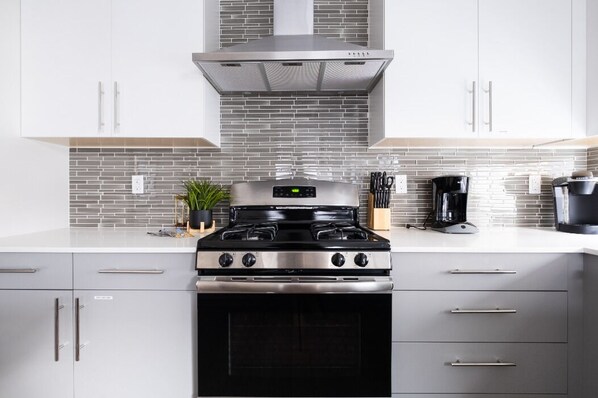 Una cocina moderna con estufa de acero inoxidable, armarios blancos y salpicadero de azulejos.