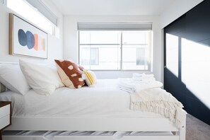 Een slaapkamer met een wit bed, een groot raam en een kunstwerk in een lijst aan de muur.