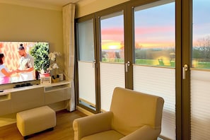 Una sala de estar con televisión, un sofá, una mesita y una ventana con persianas.