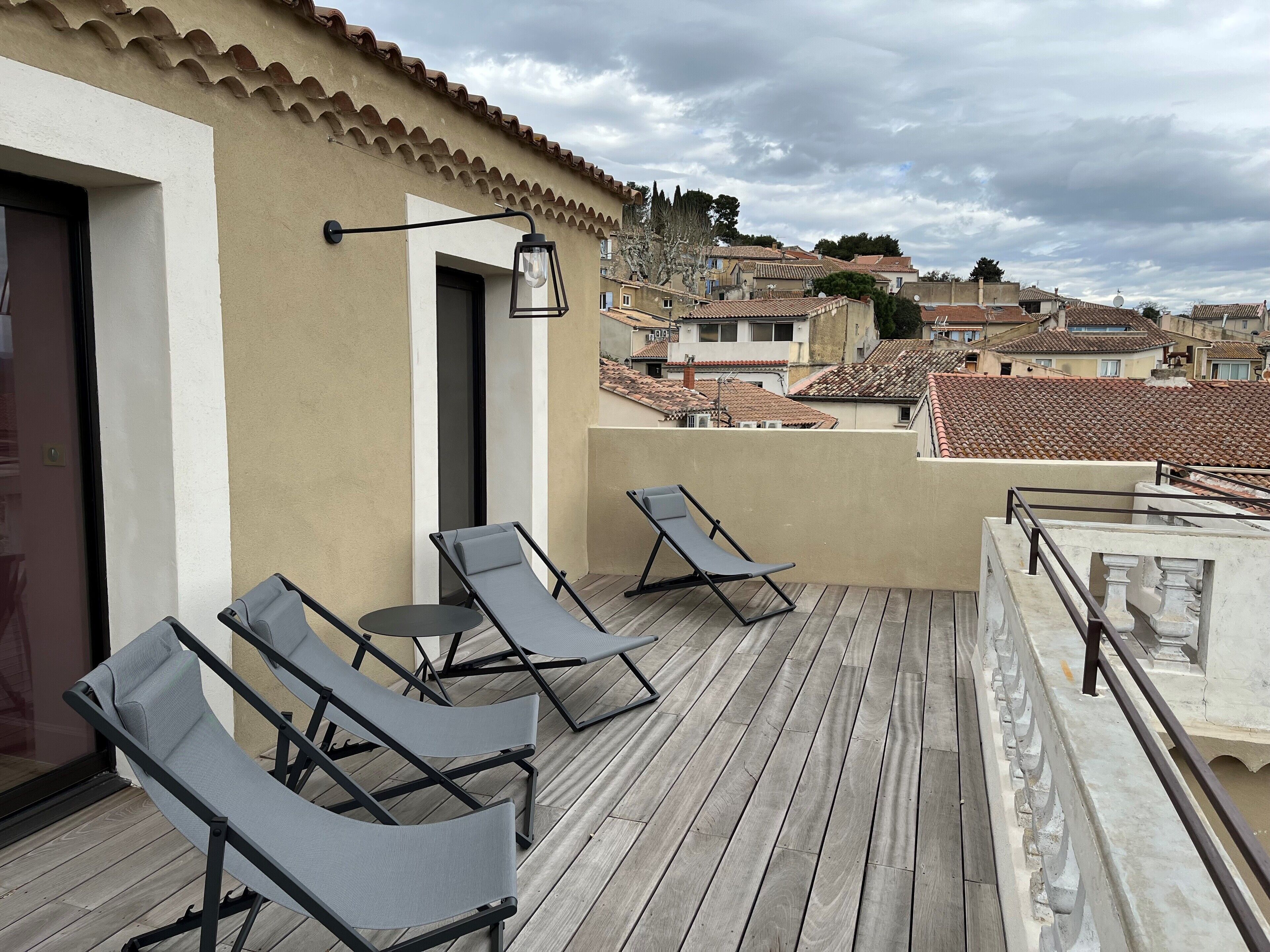 Terraza en la azotea con dos sillones y una mesa, con vistas a un barrio residencial de tejados de teja.